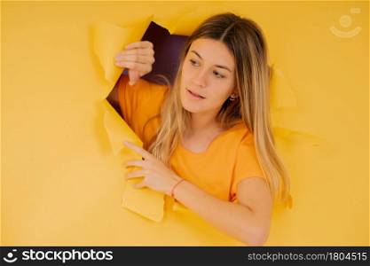Portrait of a young woman looking to the side while standing through a ripped hole in the paper wall.