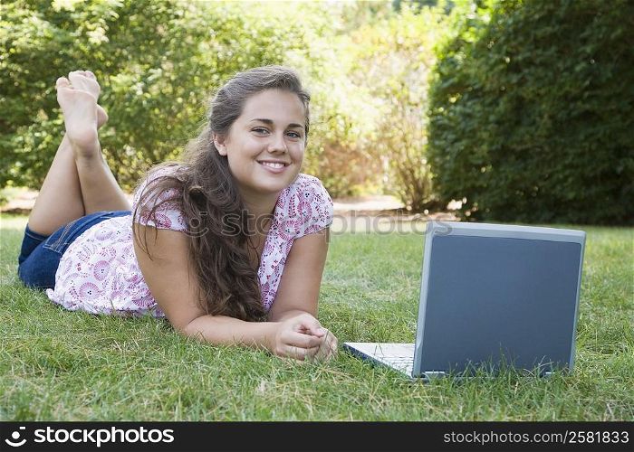 Portrait of a young woman lying in front of a laptop and smiling