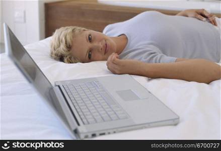 Portrait of a young woman lying on a bed beside a laptop
