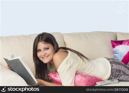 Portrait of a young woman lying on a couch and holding a book