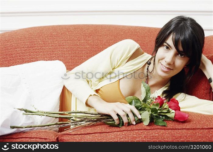 Portrait of a young woman lying on a couch and holding a bunch of flowers