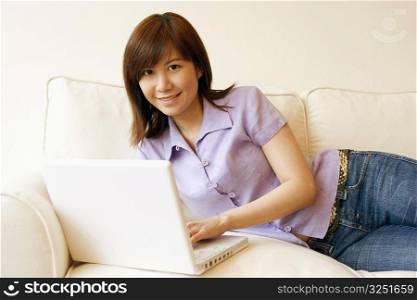 Portrait of a young woman lying on a couch and working on a laptop