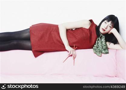 Portrait of a young woman lying on a couch holding chopsticks