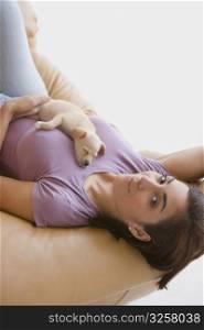 Portrait of a young woman lying on a couch with a puppy on her