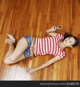 Portrait of a young woman lying on a hardwood floor and holding a mobile phone