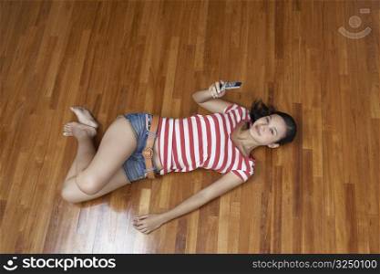 Portrait of a young woman lying on a hardwood floor and holding a mobile phone