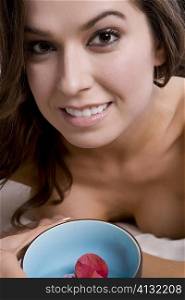 Portrait of a young woman lying on a massage table and holding a bowl