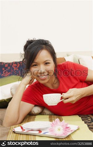 Portrait of a young woman lying on the bed and holding a cup of tea