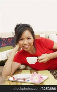 Portrait of a young woman lying on the bed and holding a cup of tea