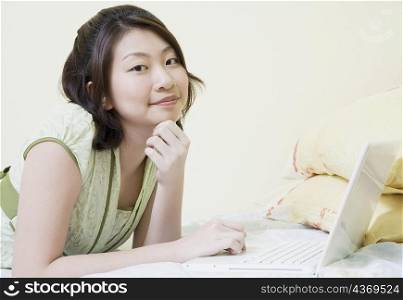 Portrait of a young woman lying on the bed and using a laptop