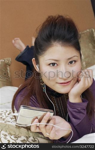 Portrait of a young woman lying on the bed listening to an MP3 player