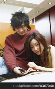 Portrait of a young woman lying on the bed with a young man holding a mobile phone