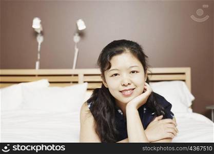Portrait of a young woman lying on the bed with her hand on her chin