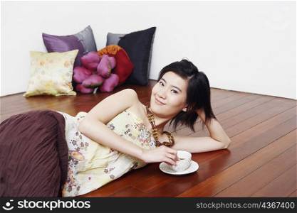 Portrait of a young woman lying on the floor and holding a cup of tea