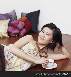 Portrait of a young woman lying on the floor and holding a cup of tea