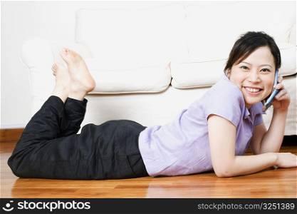 Portrait of a young woman lying on the floor and talking on a mobile phone