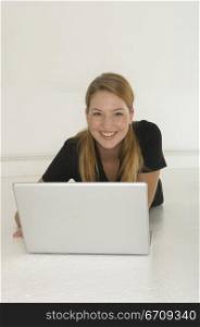Portrait of a young woman lying on the floor in front of a laptop and smiling