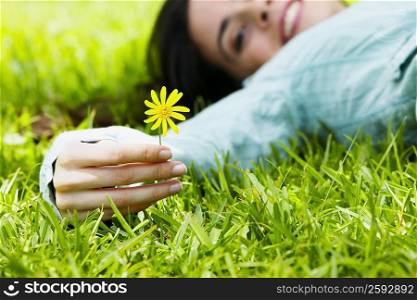 Portrait of a young woman lying on the grass and holding a flower