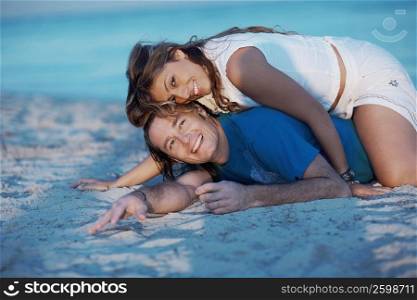 Portrait of a young woman lying on top of a mid adult man on the beach