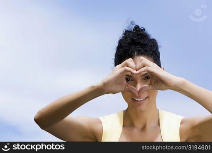 Portrait of a young woman making a heart shape in front of her face and smiling