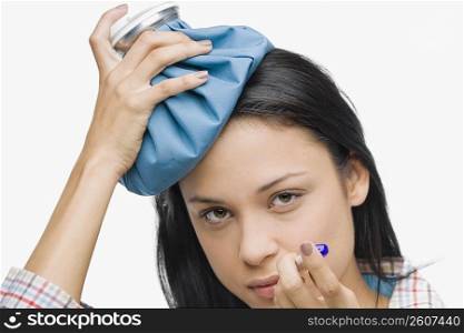 Portrait of a young woman measuring her temperature with a thermometer and holding an ice pack on her head