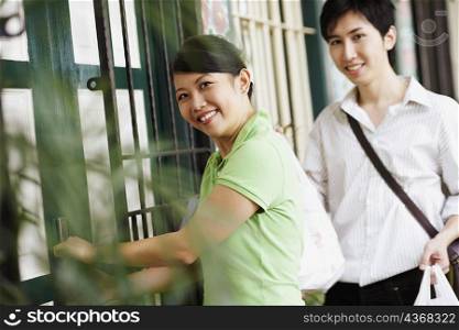 Portrait of a young woman opening a door with a young man standing beside her