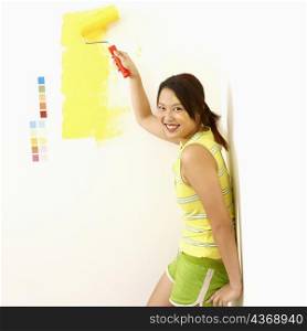 Portrait of a young woman painting a wall with a paint roller