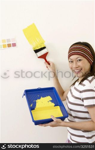 Portrait of a young woman painting a wall with a paintbrush and smiling