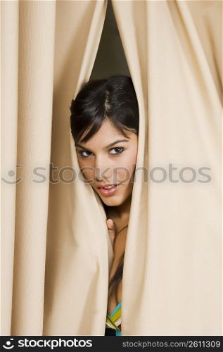 Portrait of a young woman peeking through a curtain