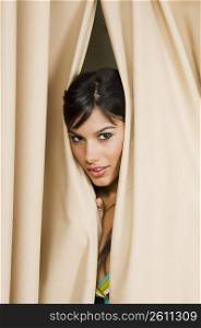 Portrait of a young woman peeking through a curtain