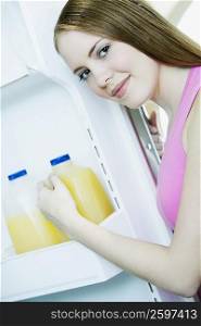 Portrait of a young woman picking out a bottle from a refrigerator