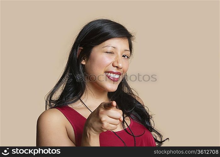 Portrait of a young woman pointing while winking over colored background