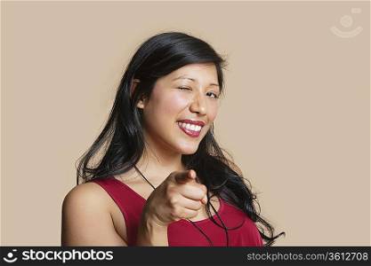 Portrait of a young woman pointing while winking over colored background
