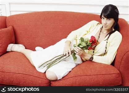 Portrait of a young woman reclining on a couch and holding a bunch of flowers