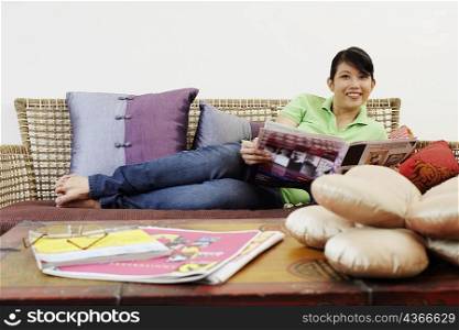 Portrait of a young woman reclining on a couch and holding a newspaper
