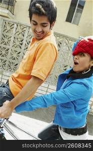 Portrait of a young woman riding a bicycle with a young man sitting on the handlebar