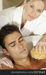 Portrait of a young woman scrubbing a young man&acute;s chest with a bath sponge