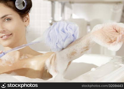 Portrait of a young woman scrubbing her arm with a bath sponge