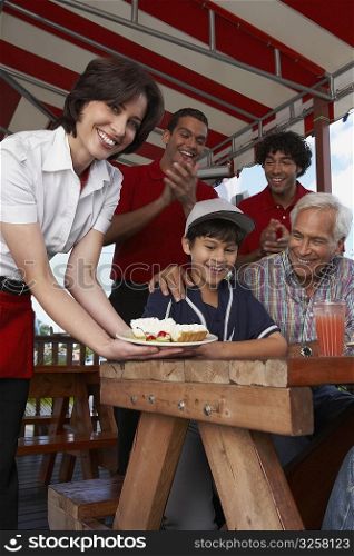 Portrait of a young woman serving dessert to a boy celebrating his birthday in a restaurant