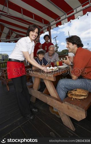 Portrait of a young woman serving dessert to a mid adult man celebrating his son&acute;s birthday in a restaurant