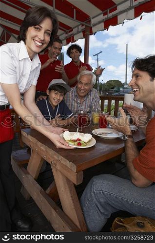 Portrait of a young woman serving dessert to a mid adult man celebrating his son&acute;s birthday in a restaurant