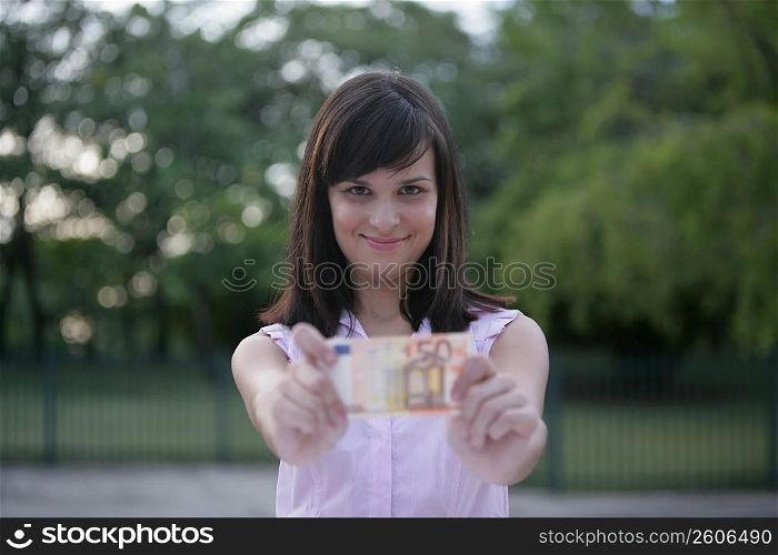 Portrait of a young woman showing a fifty Euro banknote and smiling
