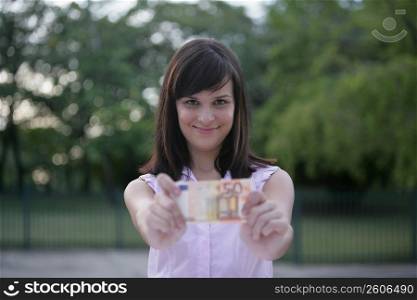 Portrait of a young woman showing a fifty Euro banknote and smiling