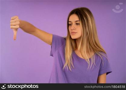 Portrait of a young woman showing a thumb down to someone while standing against an isolated background.