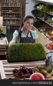 Portrait of a young woman showing a tray of wheatgrass and smiling