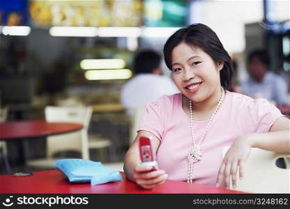 Portrait of a young woman sitting at a sidewalk cafe and holding a mobile phone