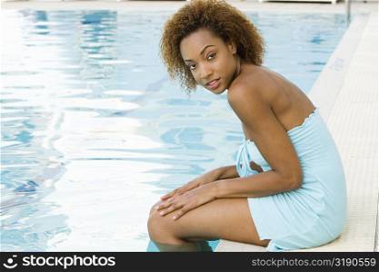 Portrait of a young woman sitting at the edge of a swimming pool