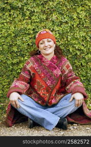 Portrait of a young woman sitting cross-legged on footpath and smiling