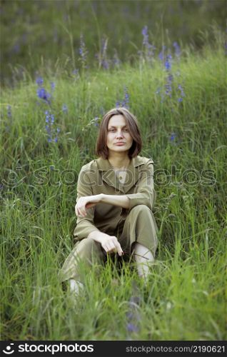 Portrait of a young woman sitting in a field on the spring grass among purple flowers. stylish girl enjoys Sunny spring weather. Natural beauty of a woman, natural cosmetics.. Portrait of a young woman sitting in a field on the spring grass among purple flowers. stylish girl enjoys Sunny spring weather. Natural beauty of a woman, natural cosmetics