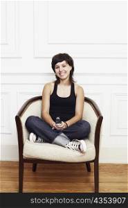 Portrait of a young woman sitting in an armchair and holding a mobile phone